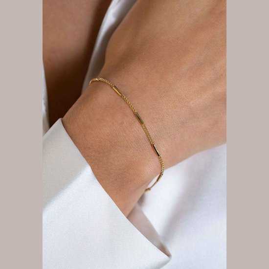Close-up van een gouden armband met buisvormige schakels, gedragen om een pols van een vrouw.