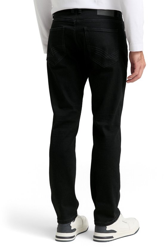 Man in zwarte jeans met witte longsleeve, staand van achteren.