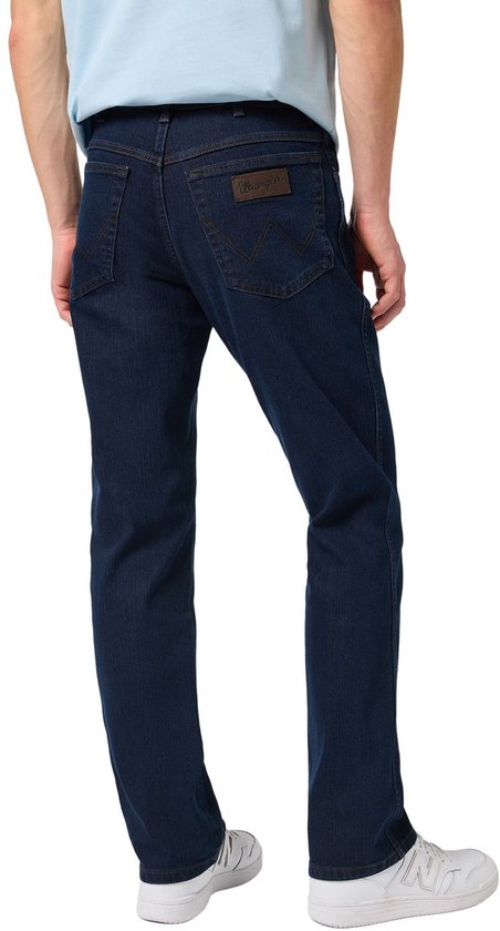 Achteraanzicht van een man in een lichtblauw T-shirt en een donkerblauwe Wrangler jeans met bruin leren merklabel.