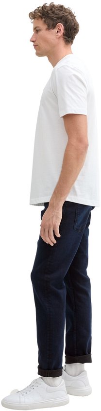 Man in een donkerblauwe jeans en een wit T-shirt, gefotografeerd vanaf de zijkant.