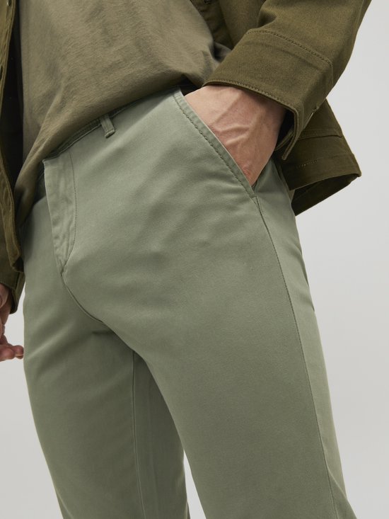 Detail van de olijfgroene chino broek met zakken, gedragen door een man.