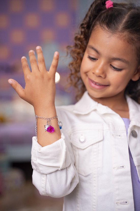 Meisje met krullend haar draagt een armband met roze hart en blauwe bedel. Ze kijkt lachwekkend naar de armband.