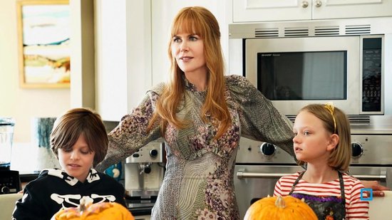 Nicole Kidman met rood haar in een bloemenjurk, staat tussen een jongen en een meisje in een keuken.