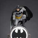Batman-figuur in grijze outfit hurkend boven de lichtgevende schijnwerper met Bat-logo.