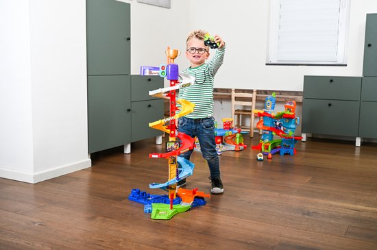 Jongen met groen-wit gestreept shirt speelt met kleurrijke racebaan met autootjes.