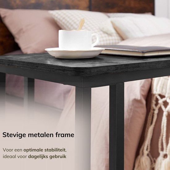 Detail van de stevige metalen frame van een zwart bijzettafeltje, naast een bed.