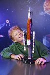 Jongen met krullend haar, kijkt met een glimlach omhoog naar een LEGO Technic NASA Artemis ruimtevaartuig met gouden en witte details.