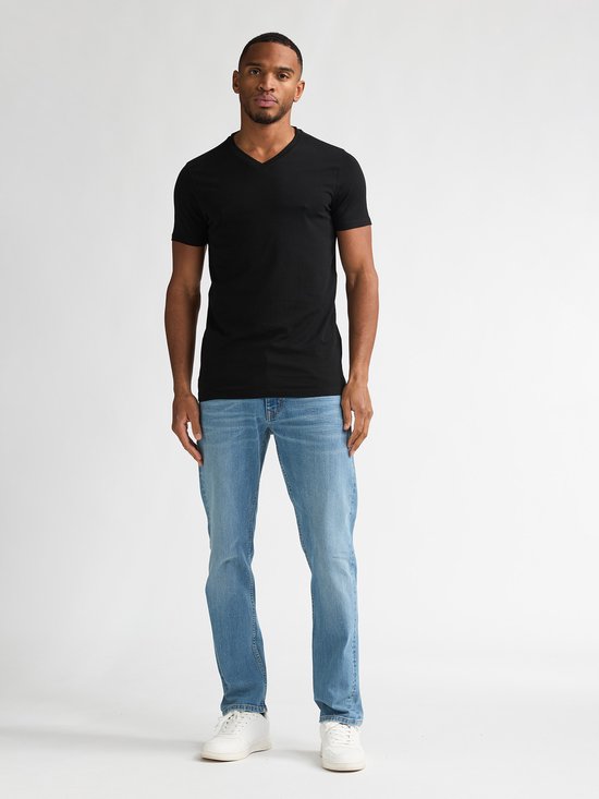 Man met donkere huid, met korte zwarte V-hals T-shirt en lichtblauwe jeans, witte sneakers.