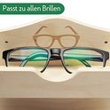 Zwarte bril met groene glazen rustend in een houten brillenhouder met een gegraveerd bril-icoon.