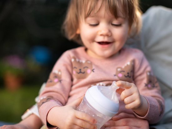 Een baby met een roze trui met beren, die een fles met een Philips Avent speen vasthoudt.