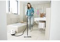 Femme utilisant un nettoyeur vapeur dans une salle de bain carrelée de blanc.
