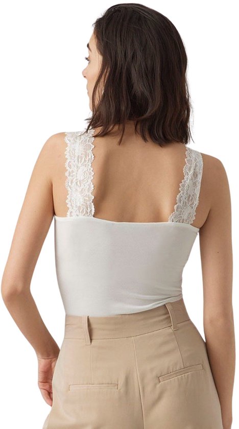 Zijaanzicht van model in wit kanten hemdje met V-hals, beige wijde broek.