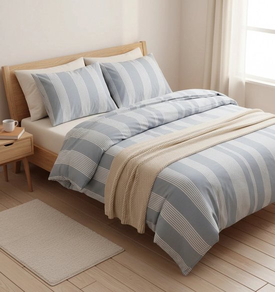 Blauw dekbedovertrek met fijne witte strepen, op een bed met een houten hoofdeinde en een gebreide plaid.