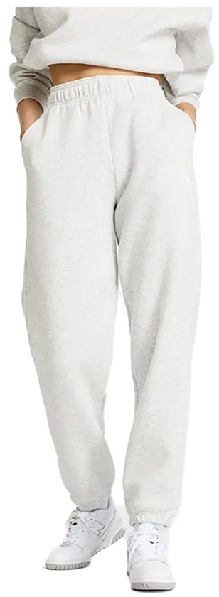 Een model staat in een lichtgrijze joggingbroek met trekkoord en bijpassende crop top en sneakers.