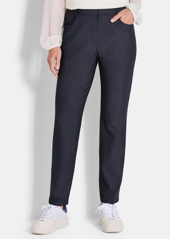 Model in een donkerblauwe, aansluitende broek met steekzakken, tot op de enkel.