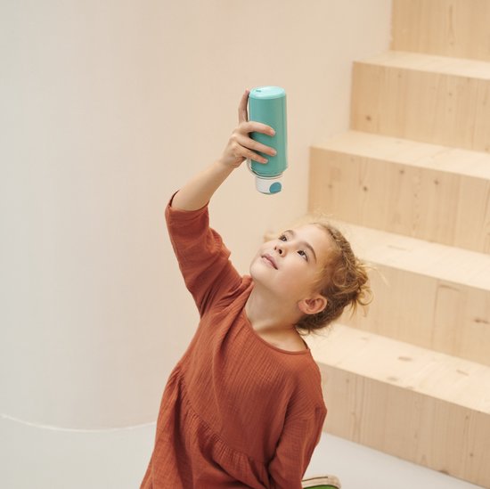 Une fille regarde une gourde bleu clair qu'elle tient à la main.