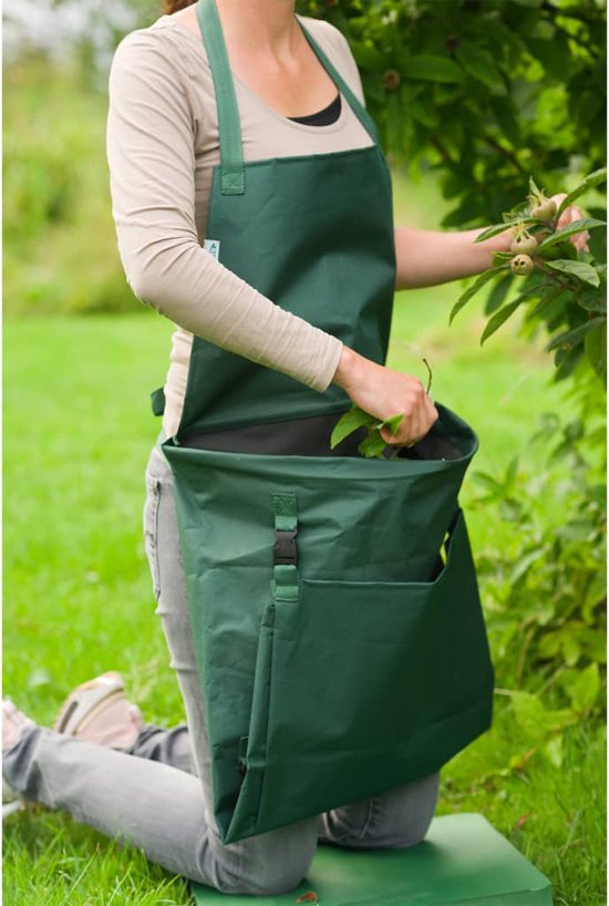 Vrouw met groen tuig en opvangzak, bladeren erin aan het doen, geknield.