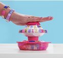 Hand met paarse en blauwe armbandjes gebruikt de Pop Style armbandjesmaker, met gouden accenten.