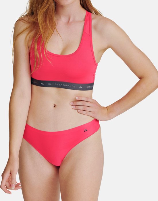 Model draagt een felroze sportbeha en slip. De beha heeft een grijze band met logo.