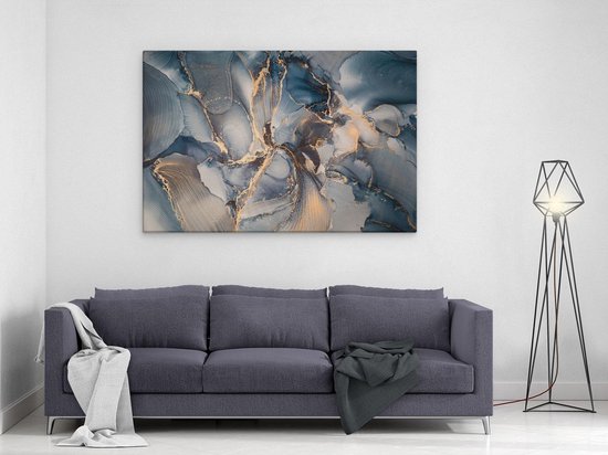 Tableau abstrait aspect marbre bleu, gris et or, suspendu au-dessus d'un canapé gris foncé avec des plaids.