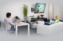 Een zwenkbare tv-muurbeugel gemonteerd aan de muur, met een tv erop. Een man leest aan een tafel, een vrouw zit op de bank.
