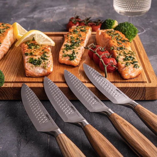 Vier Boska RVS steakmessen met houten handvatten liggen op een plank met gegrilde zalm.