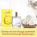 Een parfumflesje Eau de Zwitsal met gele doos, opgemaakte tafel met opgerolde handdoeken.