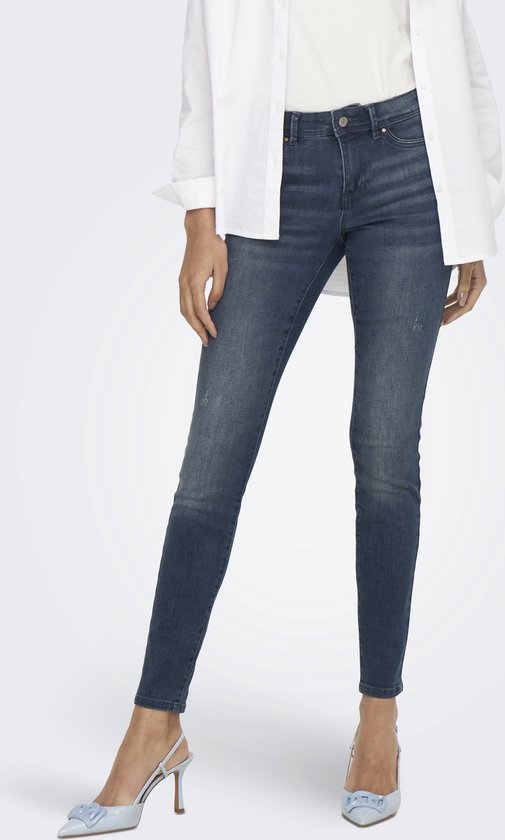 Dames in een donkerblauwe skinny jeans met lichte wassing, gedetailleerde naden en scheurtjes. Witte blouse en lichtblauwe pumps.