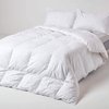 Een witte donsdeken met een vierkant stikselpatroon, opgemaakt op een bed met twee witte kussens.