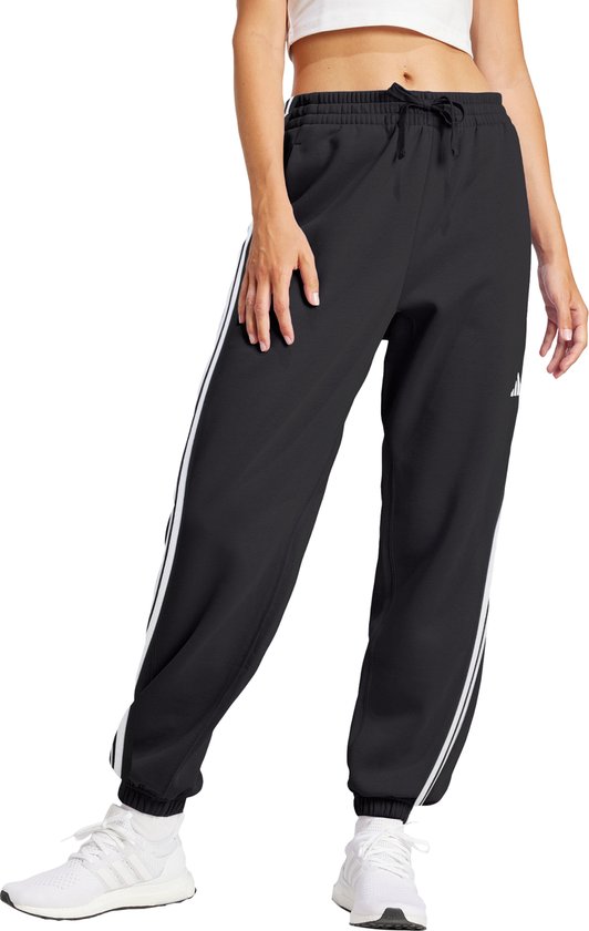 Model in zwarte joggingbroek met witte Adidas strepen, sportbeha en witte sneakers.