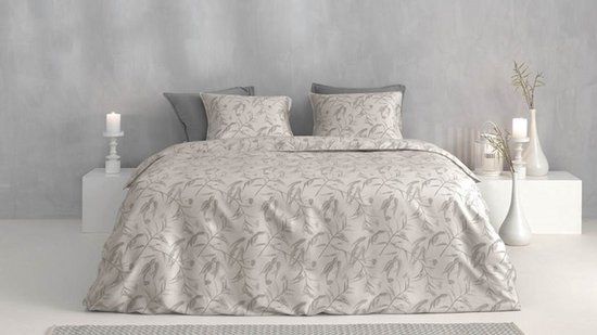 Een tweepersoonsbed opgemaakt met een lichtbeige dekbedovertrek met een grijs gebladerte patroon. Twee grijze kussens liggen achter twee bijpassende kussenslopen.