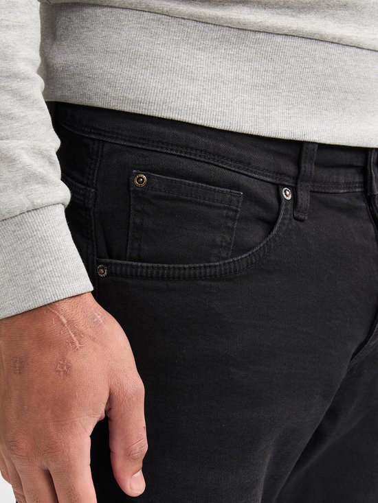 Detail van een zwarte jeans met zak, knoopsluiting en label.