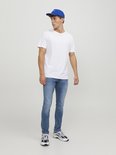 Man in witte t-shirt, blauwe pet en een lichtblauwe skinny jeans.