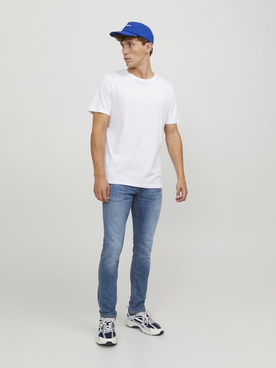 Man in witte t-shirt, blauwe pet en een lichtblauwe skinny jeans.