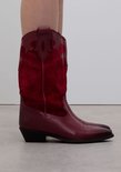 Rode leren cowboylaars met suède schacht en sierstiksels, gedragen door een model.