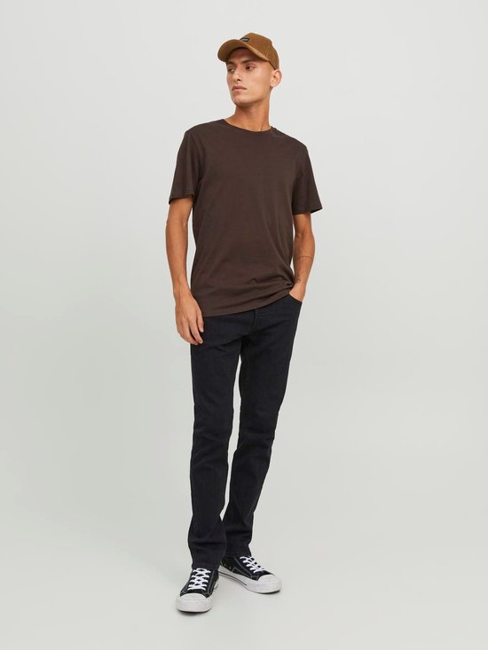 Man met bruine t-shirt, zwarte jeans, bruine pet en sneakers. Zwart denim.