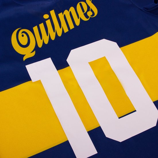 Detail van een blauw voetbalshirt met een gele horizontale band. 'Quilmes' en het witte nummer '10' zijn zichtbaar.