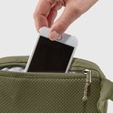 Hand plaatst smartphone in een gaasvak van een olijfgroene heuptas.