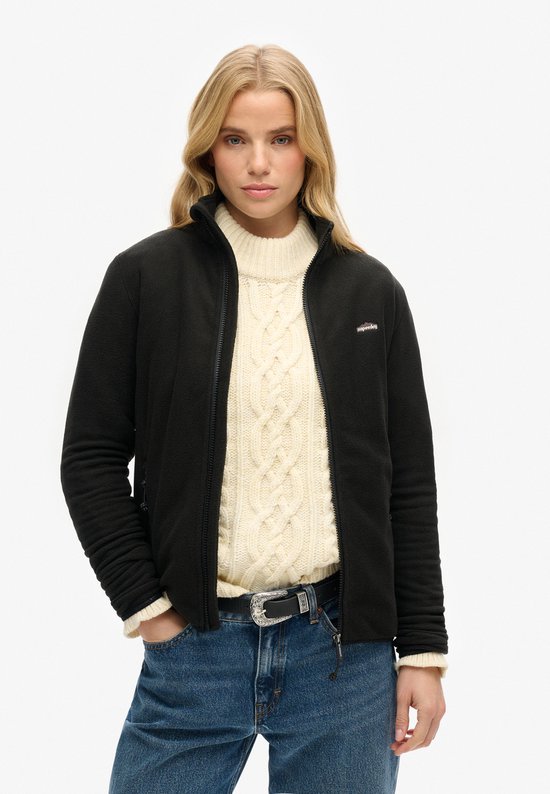 Mannequin portant une veste polaire noire zippée, pull à col roulé en tricot, jean et ceinture.