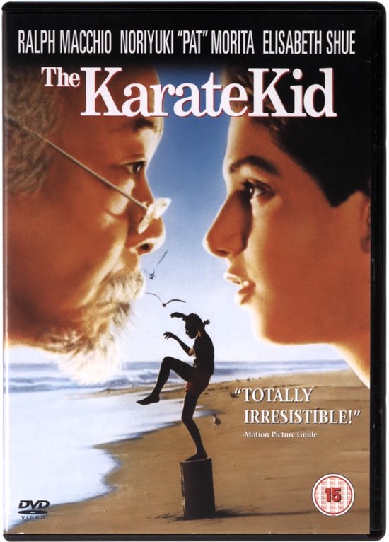 De voorkant van de DVD van The Karate Kid, met een close-up van de gezichten van Ralph Macchio en Pat Morita. Een klein figuurtje geeft een trap op een kistje op een strand.