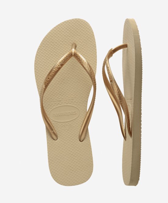 Lichtbruine Havaianas slippers met goudkleurige bandjes, op een witte achtergrond.