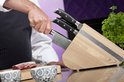Hand pakt een mes uit een houten messenblok, met vlees en kommen op de voorgrond.