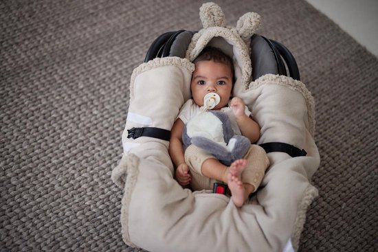 Crèmekleurige teddy wikkeldeken met konijnenoren en flapjes, om een baby in een autostoel te wikkelen.