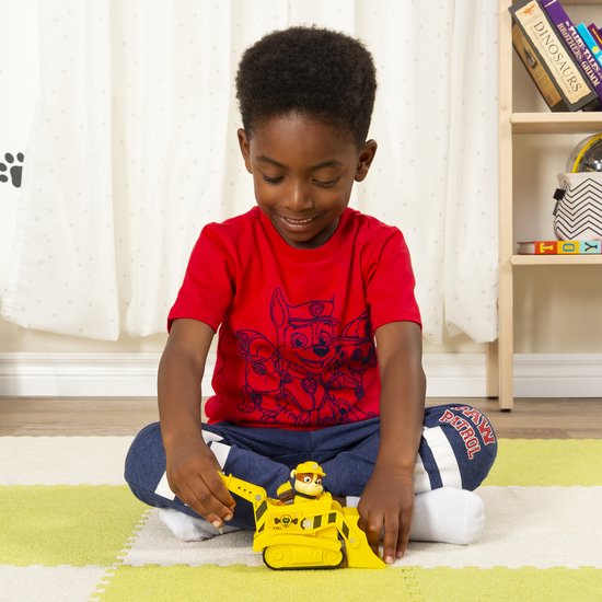 Een jongen speelt op de vloer met een gele Paw Patrol bulldozer, met Rubble erin.