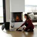 Vrouw poetst de vloer bij een brandende open haard met de grijze haardset ernaast.
