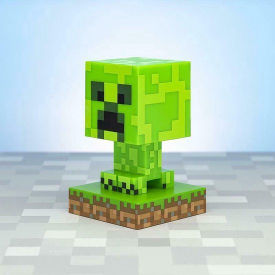 Een pixelachtige, felgroene Minecraft Creeper-lamp op een gras- en aarde-voetstuk.