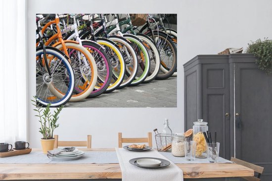 Une rangée de vélos colorés avec des jantes orange, bleues, blanches, roses et jaunes, au-dessus d'une table à manger.
