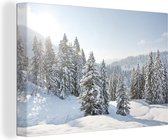 Canvas Schilderij De zon schijnt op de besneeuwde bomen bij een winterlandschap - 120x80 cm - Wanddecoratie