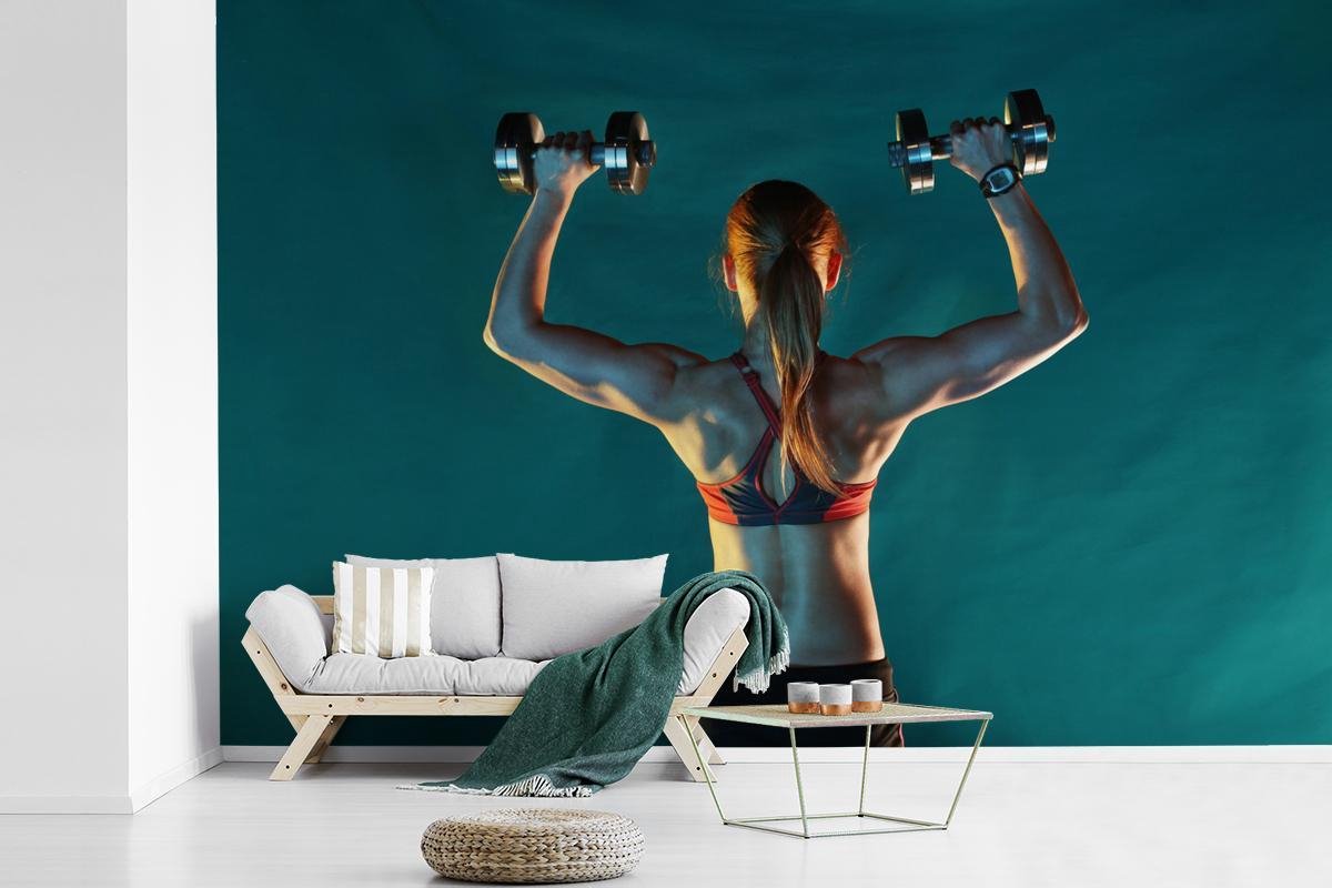 Behang - Fotobehang Een vrouw houdt twee gewichten omhoog tijdens fitness - Breedte 390 cm x hoogte 260 cm