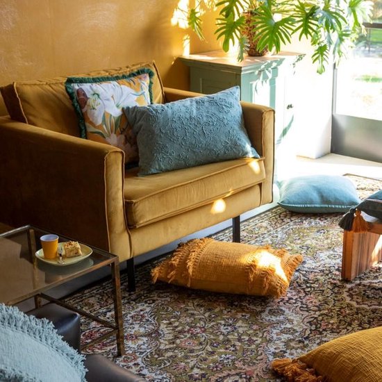 Coussin décoratif ocre avec franges sur un fauteuil avec des coussins jaunes.